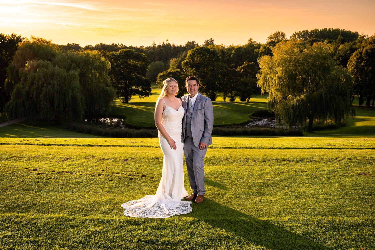 A romantic wedding portrait at sunset with rolling hills and weeping willows in the background.