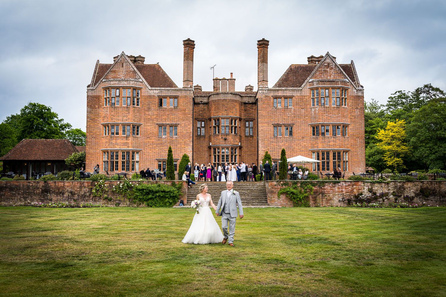 Wedding celebration at an elegant red brick English manor house with manicured lawns and historic architecture.