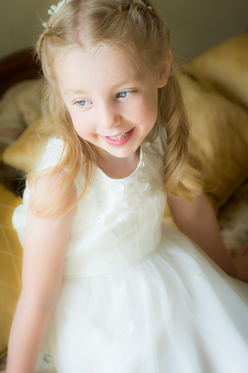 Sweet portrait of a child in a white dress with blonde pigtails against a soft blurred background.