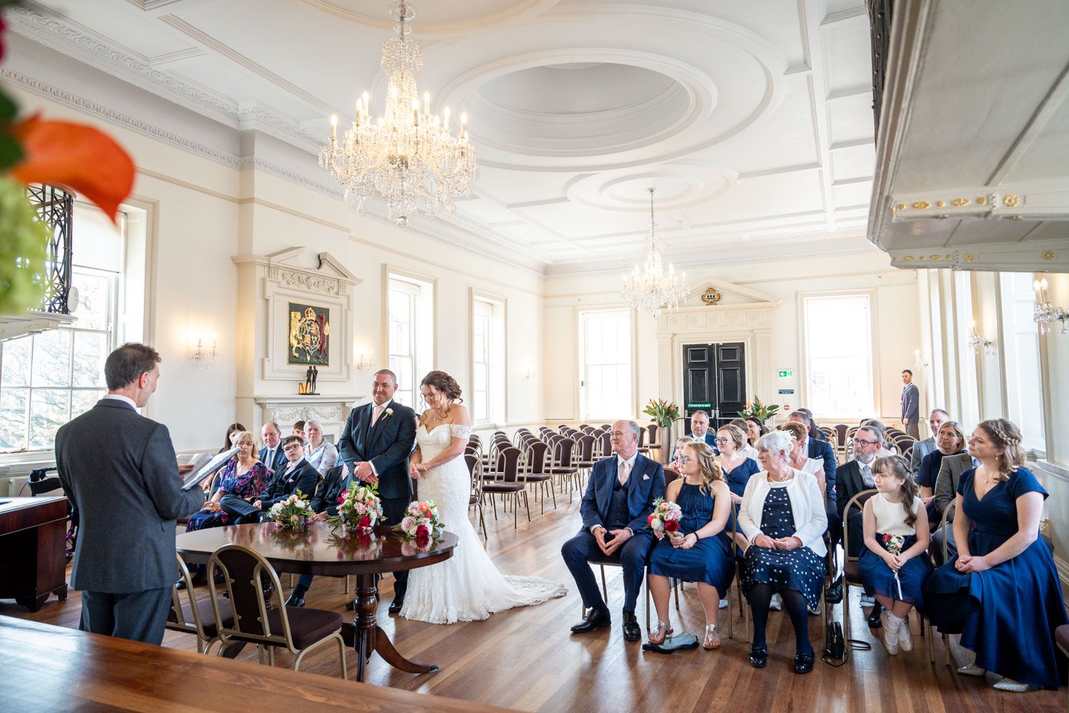 A formal event in an elegant ballroom with chandeliers and ornate white moldings as guests gather for a ceremony.