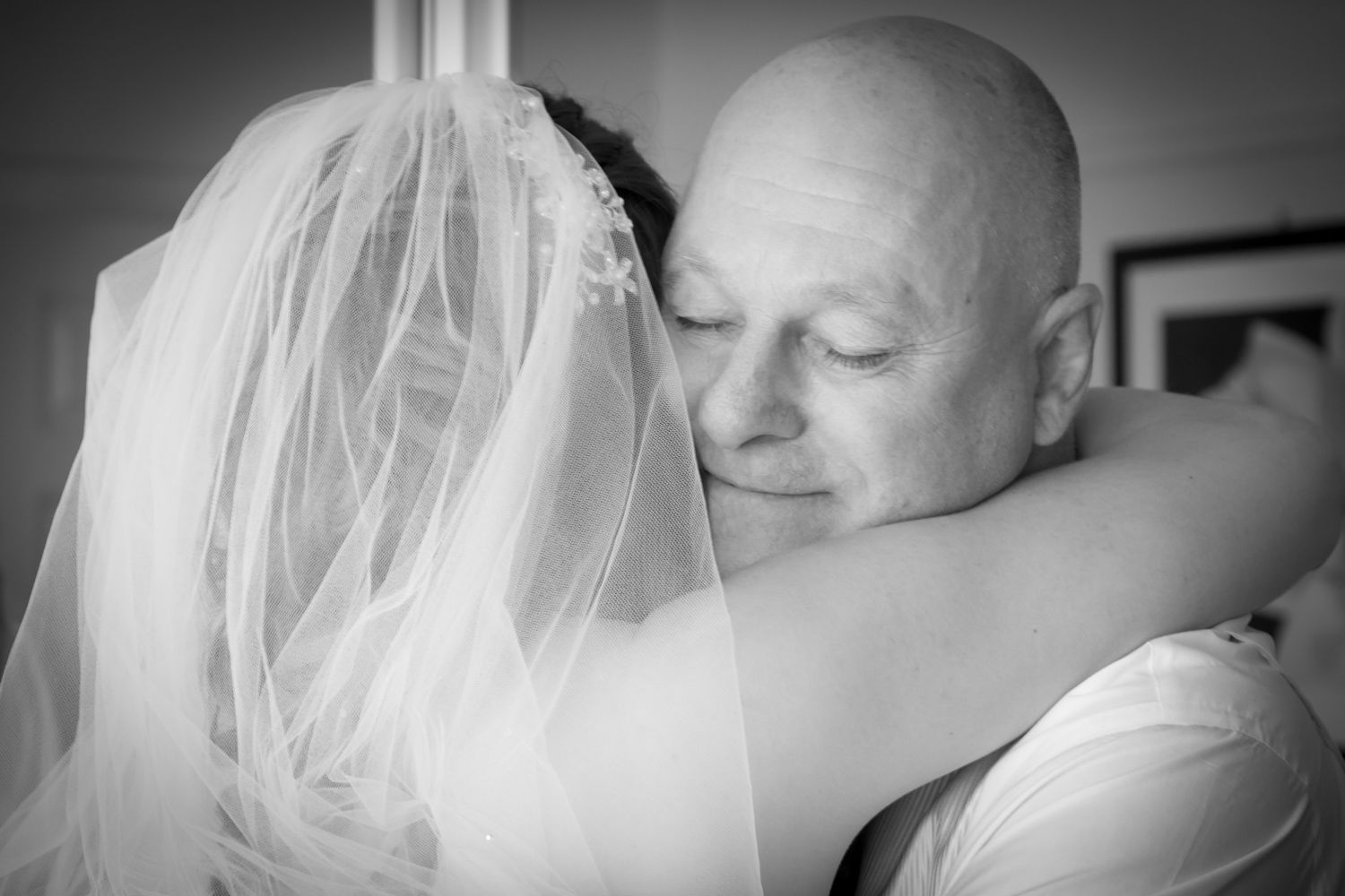 A tender black and white moment captured at a wedding as a bride in a veil embraces someone warmly.