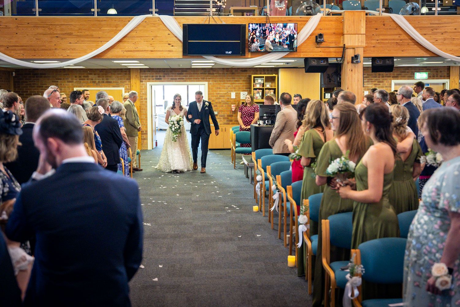 Bride walks down the aisle with escort as guests watch in a decorated wedding ceremony venue.