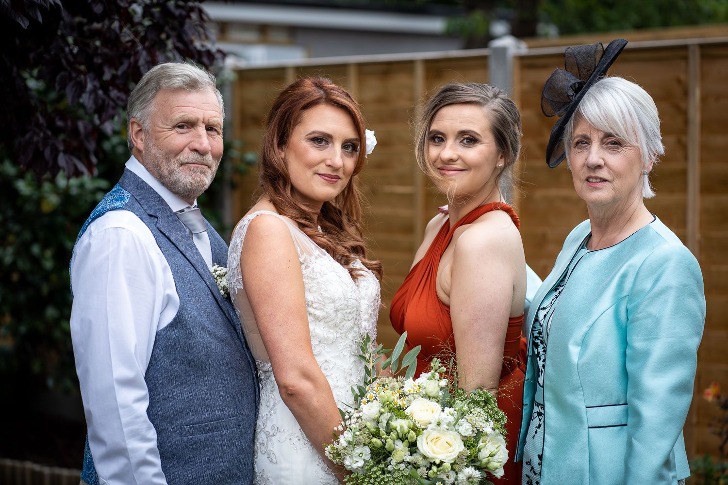 Wedding party poses outdoors on special day, bride in white holds bouquet of light-colored flowers.