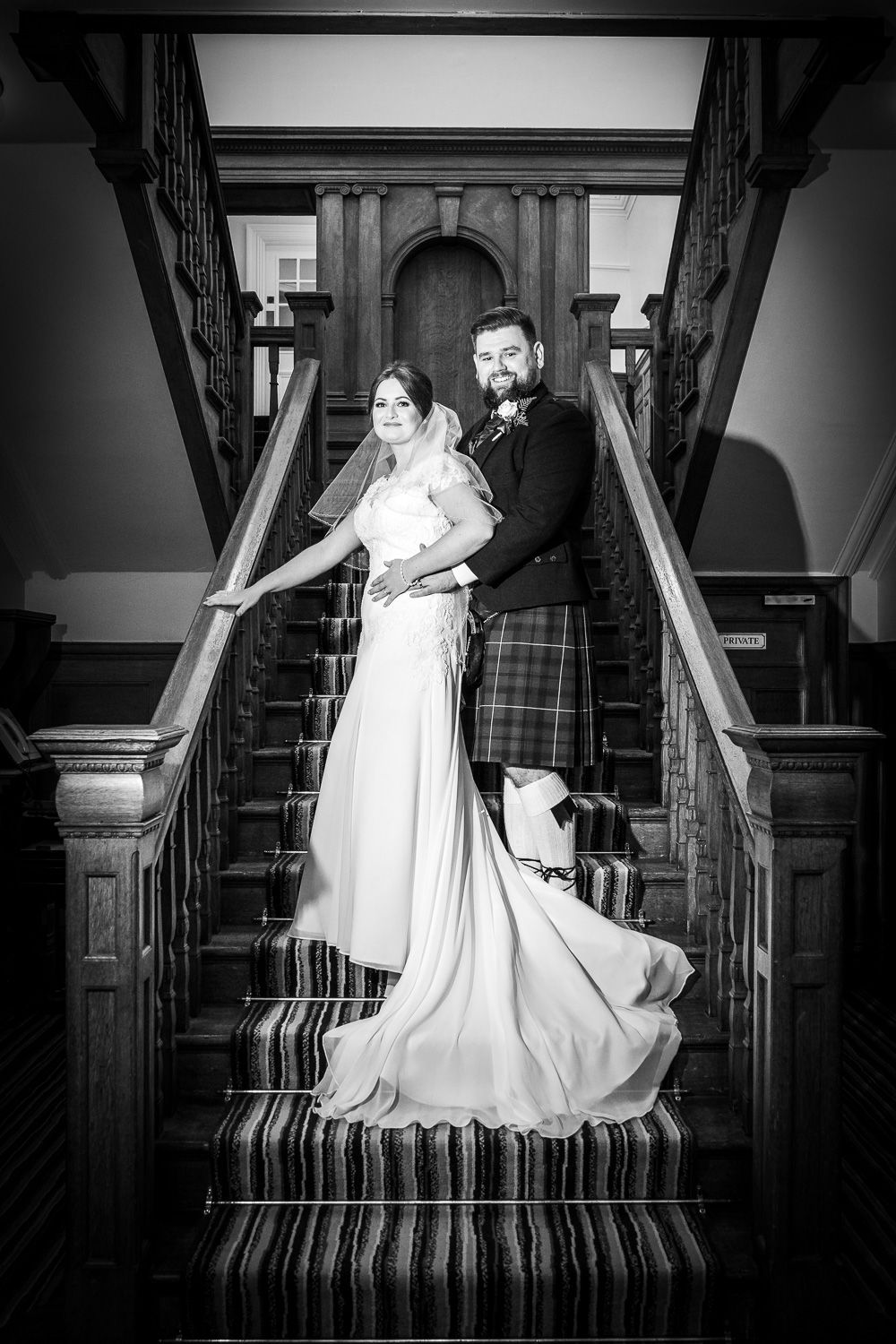 Elegant wedding portrait on grand staircase featuring traditional Scottish attire.