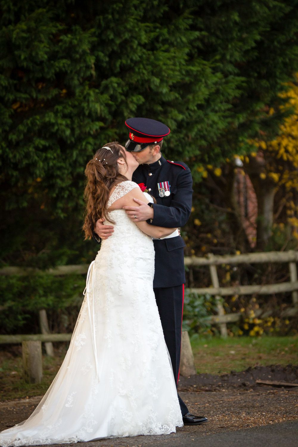A romantic wedding moment with a bride in a white gown and groom in military dress uniform embracing outdoors.