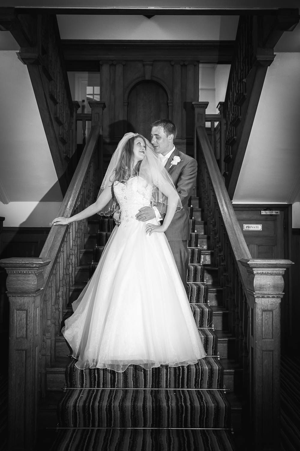 Romantic black and white wedding portrait of newlyweds posing on a vintage wooden staircase with striped carpet.