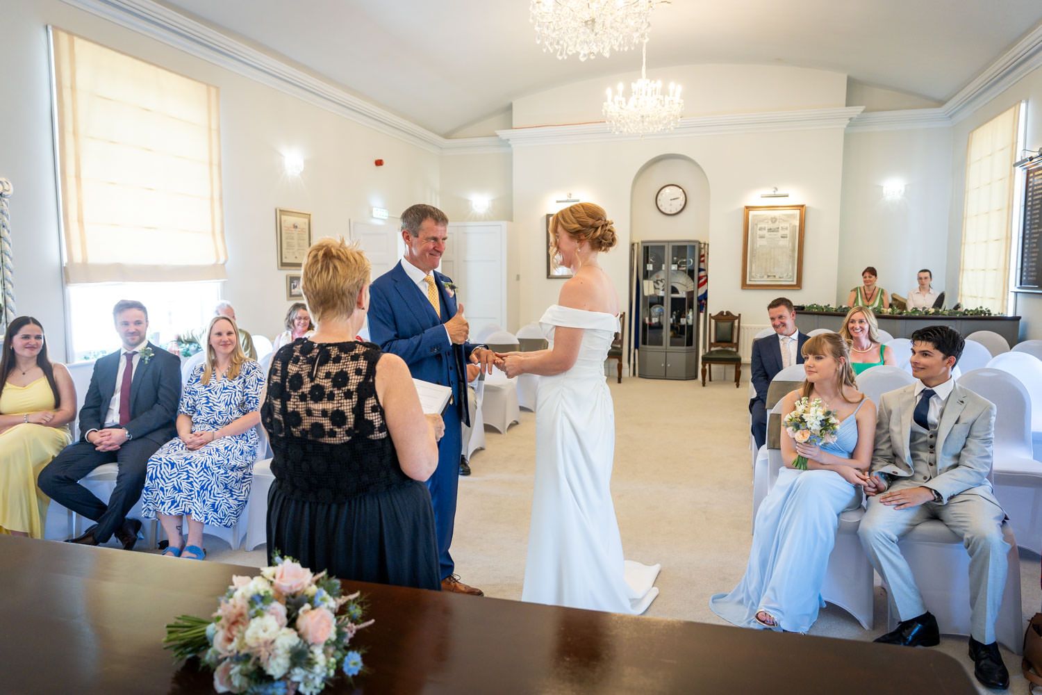 Bride and groom exchanging vows during an intimate indoor wedding ceremony with seated guests.