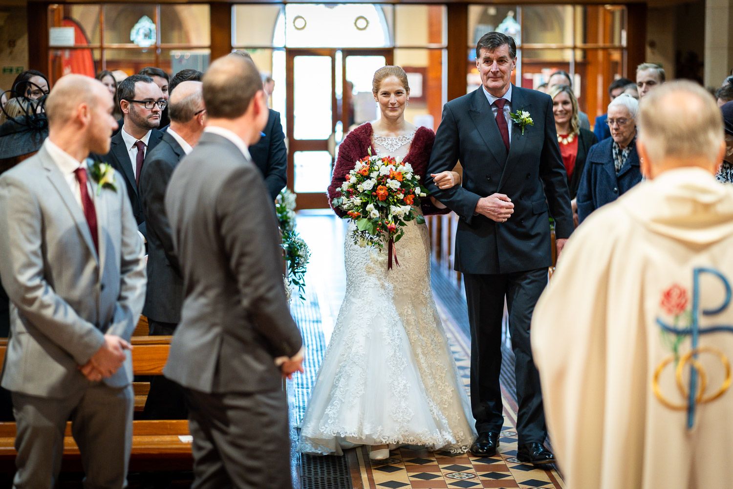 A couple walks down the church aisle during their wedding ceremony surrounded by guests and clergy.