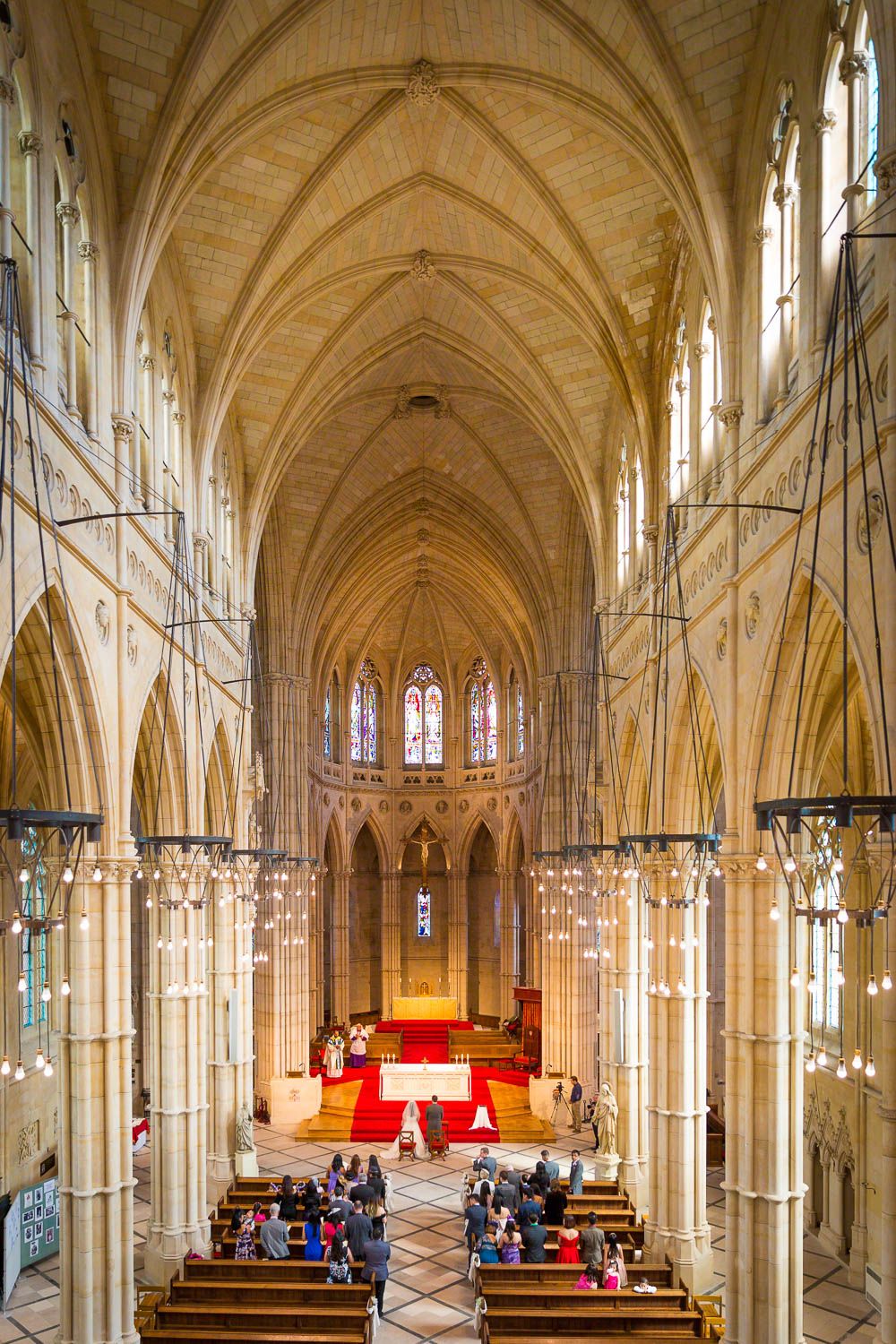 Interior view of a Gothic cathedral with vaulted ceilings, stained glass windows, and people gathered for a church service.