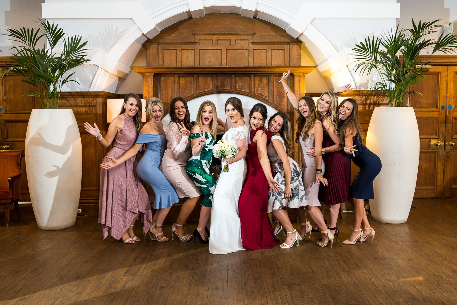 A group strikes a fun pose at a wedding celebration in front of wooden doors and decorative white vases.