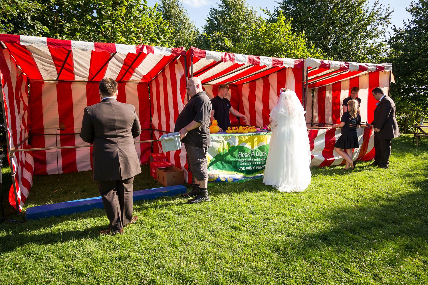 Red and white striped carnival tent booths set up on green grass lawn for an outdoor summer event or celebration.