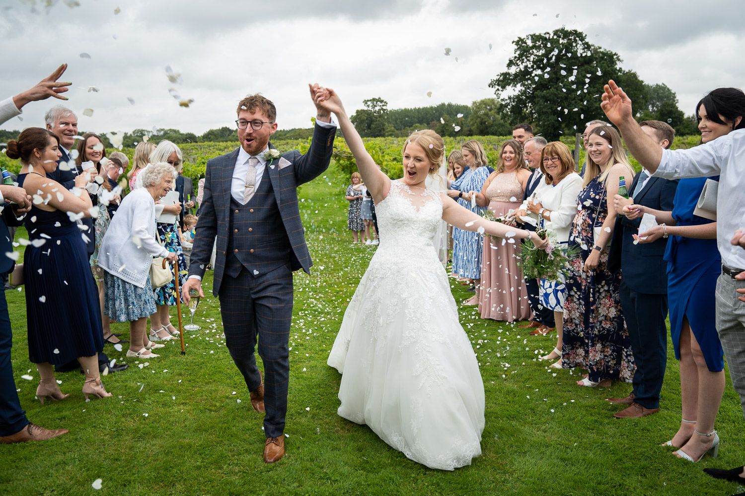 Wedding guests line up on grass path and wave as newlyweds walk through celebrating their special moment together.
