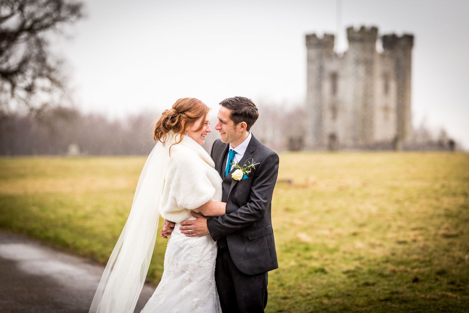 Romantic couple embraces near historic castle ruins in winter wedding portrait.