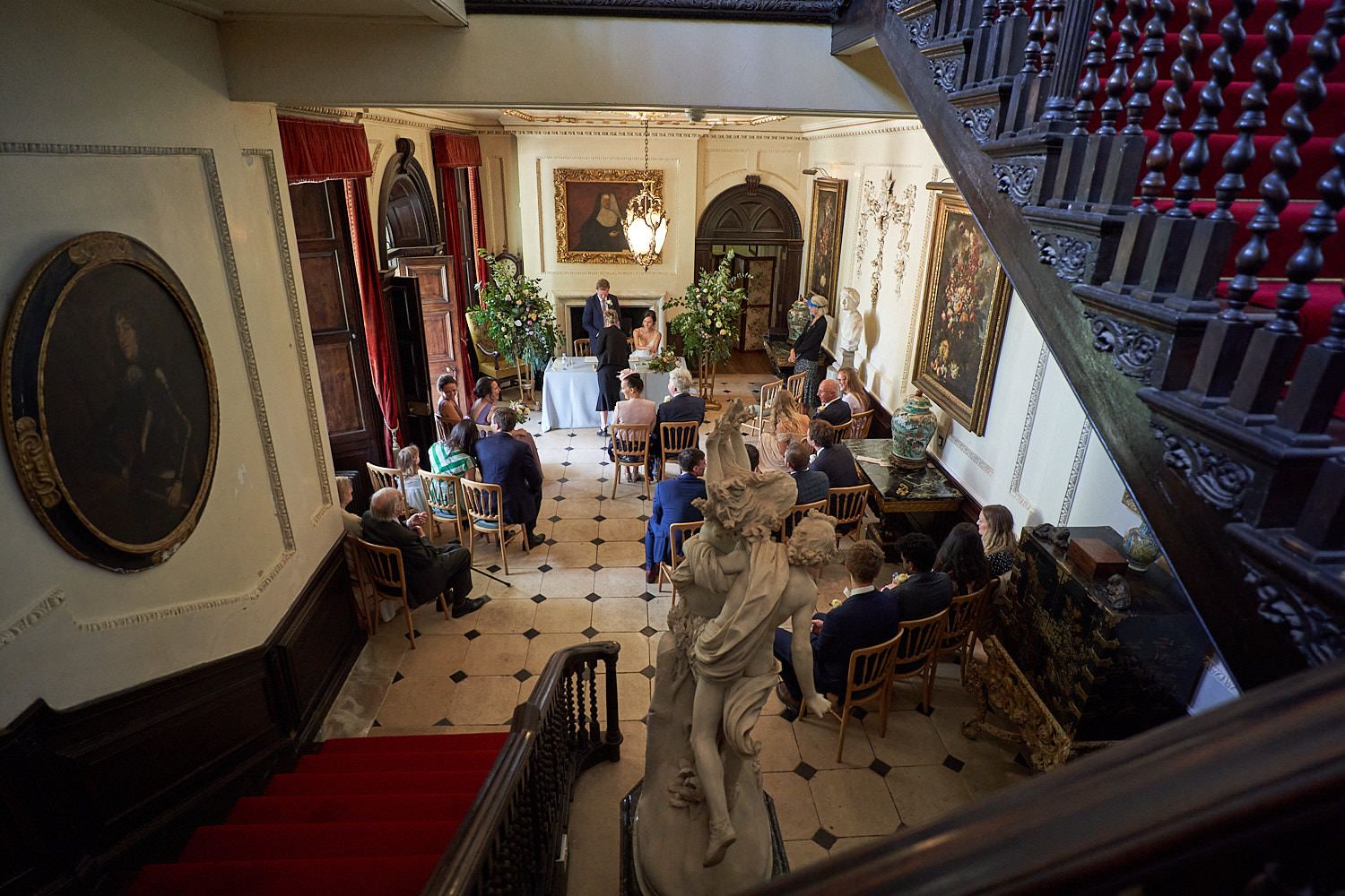 Wedding guests gather in a historic mansion foyer with checkered floors and ornate architectural details.