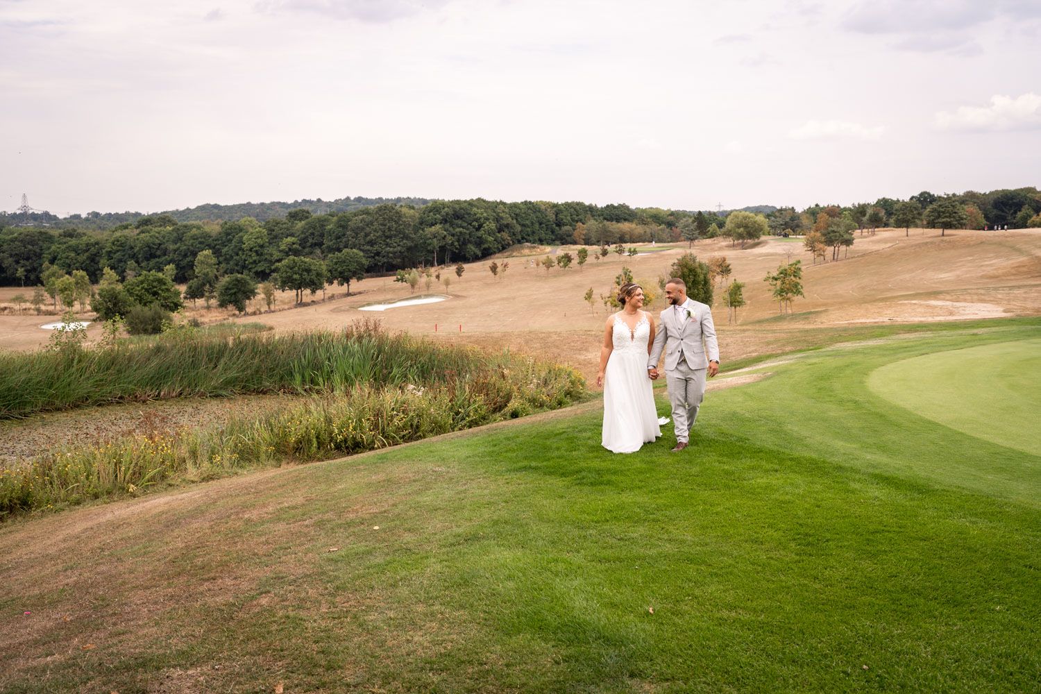 A couple walks hand in hand along a scenic golf course path surrounded by rolling hills and trees.