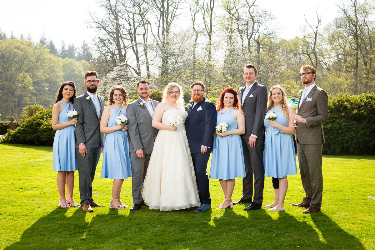 A wedding party in blue dresses and gray suits poses on a green lawn wearing matching bright yellow boots.