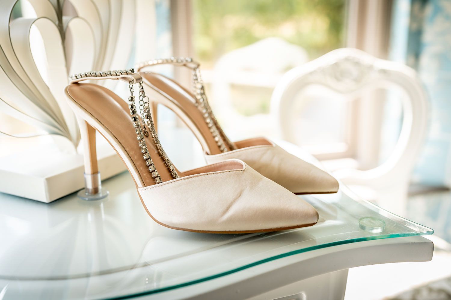 Elegant white bridal heels with crystal embellishments displayed on a glass shelf.