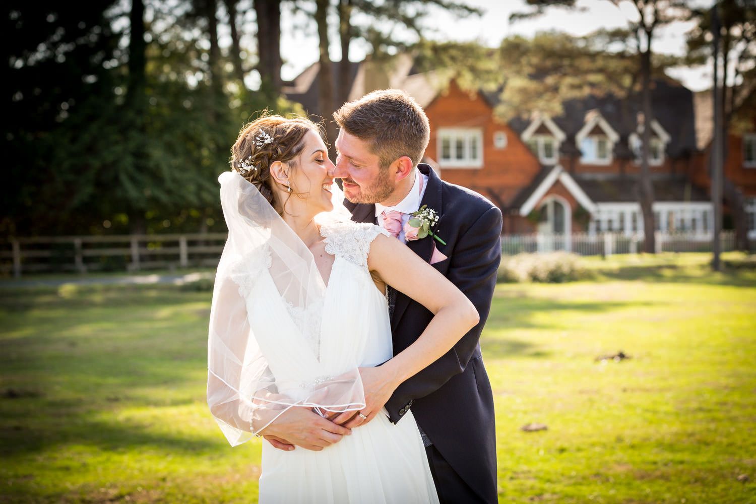 Couple shares intimate moment on sunlit lawn before charming country house.