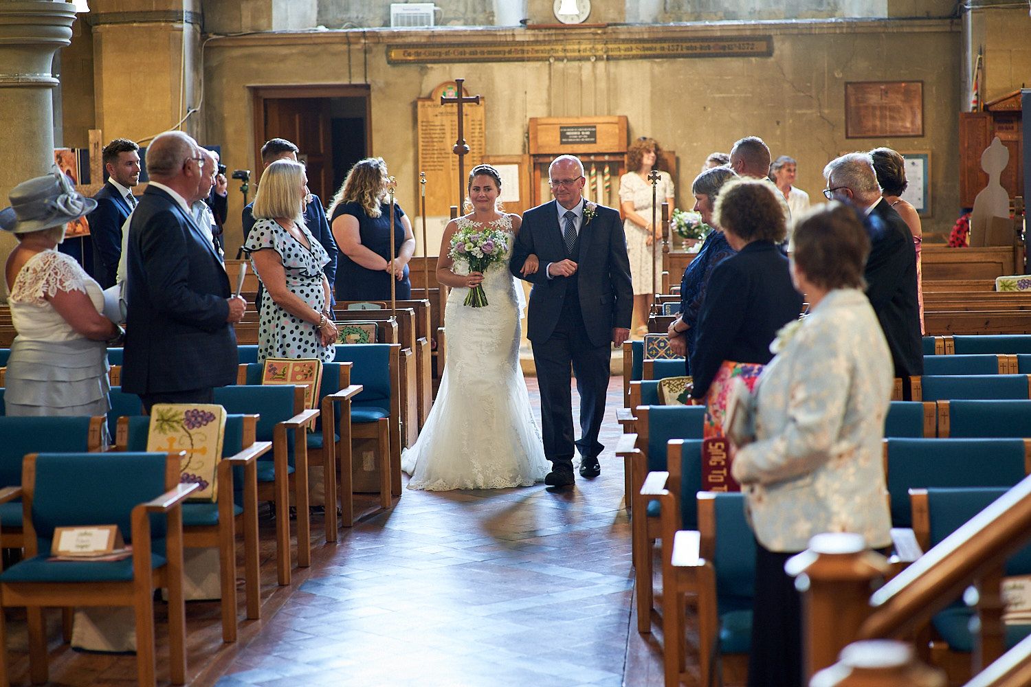 Wedding ceremony in progress inside a traditional church with wooden pews and guests looking on from the sides.