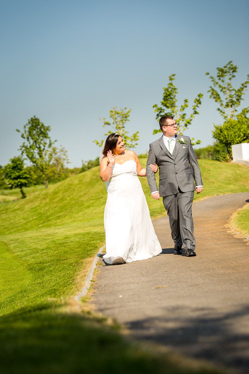 A couple walking together on a paved path at a scenic hilltop golf course on their wedding day.
