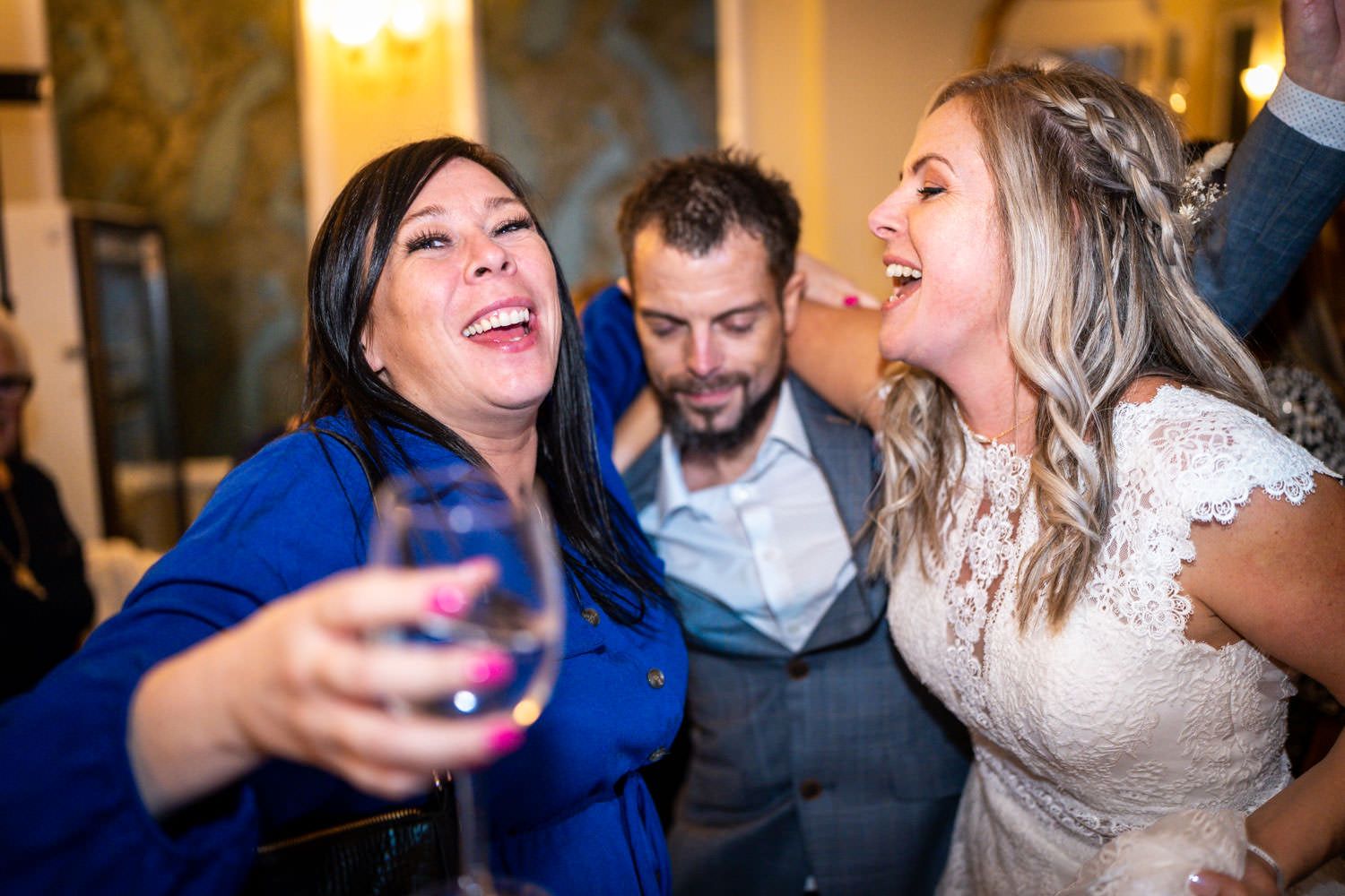 People joyfully celebrate at a wedding reception while holding drinks and laughing together.