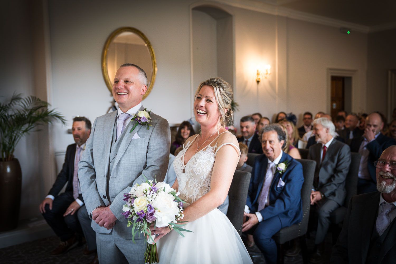 A couple sharing a joyful laugh during their wedding ceremony while guests look on from church pews.