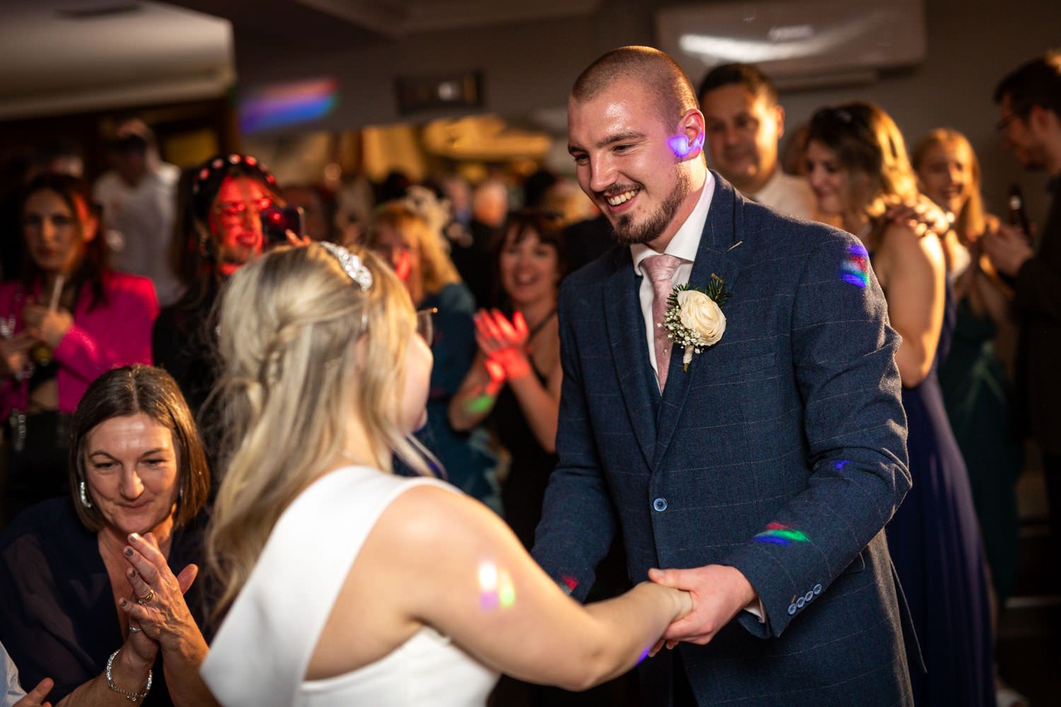 Couple dancing together during their celebration with guests smiling and watching in the background.