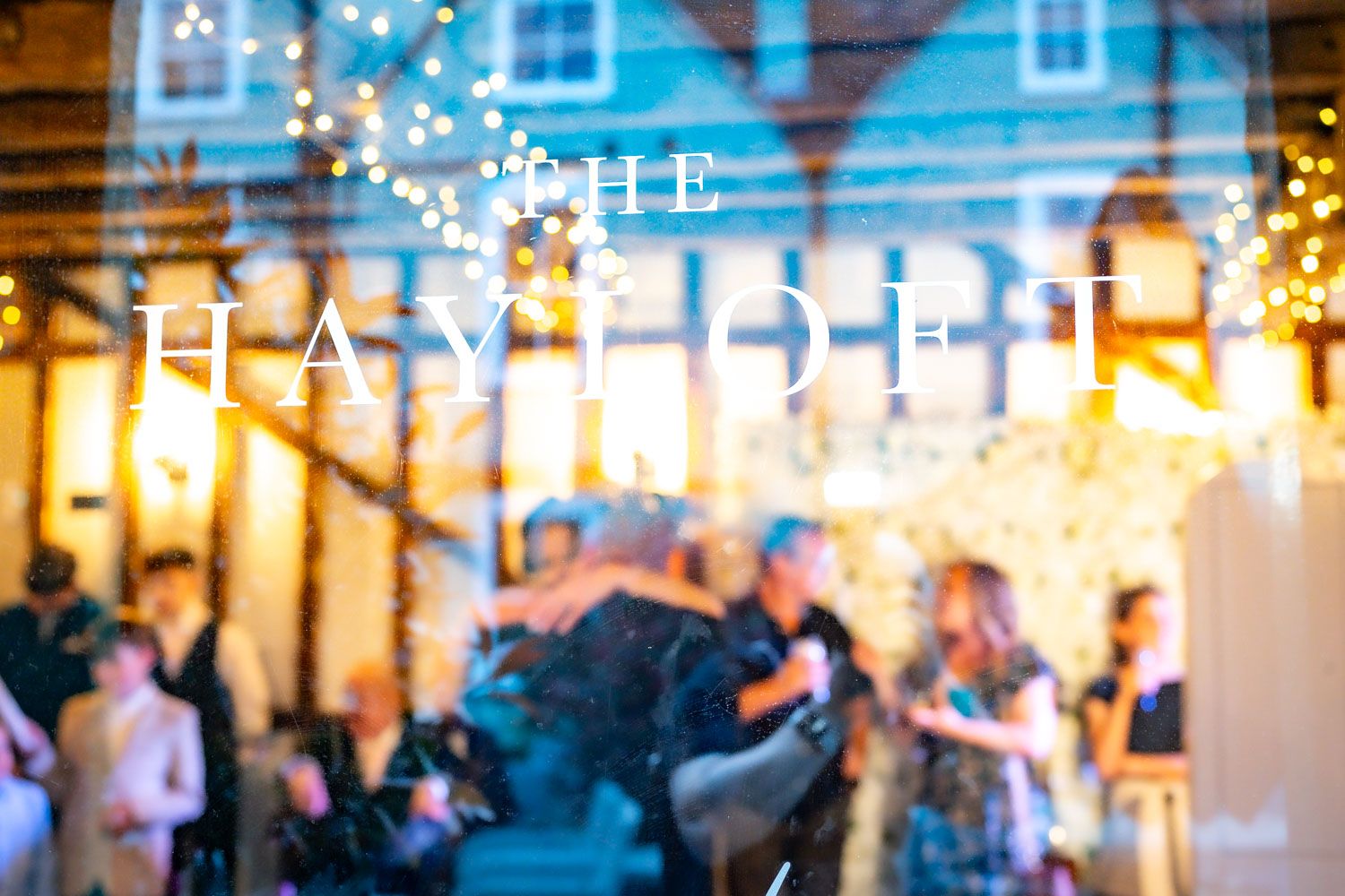 Blurred outdoor restaurant patio scene with glowing string lights and diners enjoying an evening meal in warm ambiance.