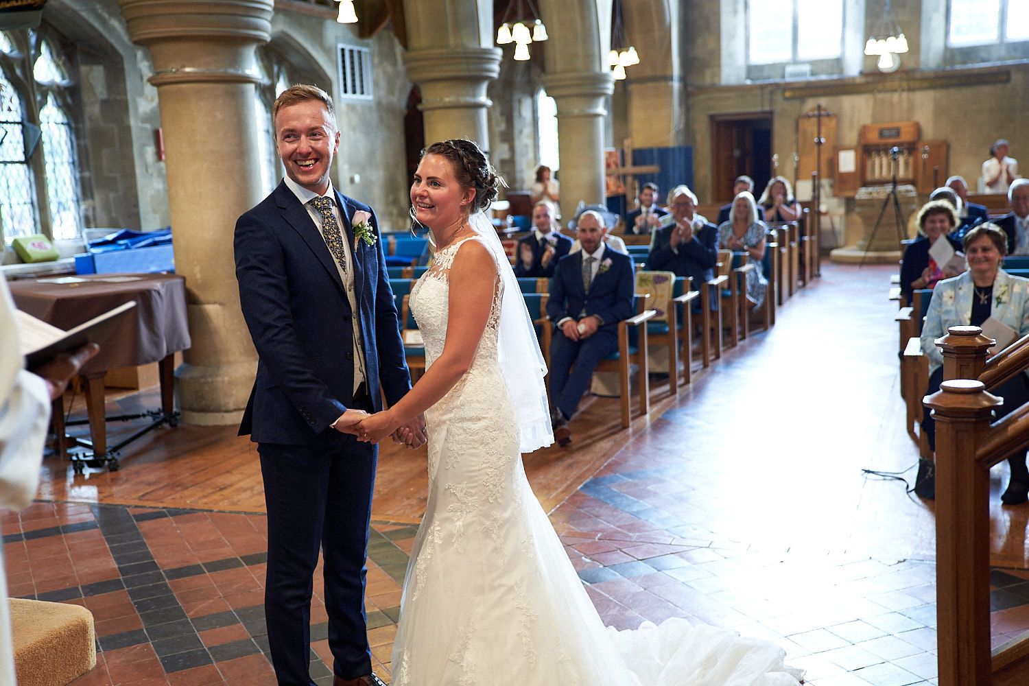 A couple standing at the altar in a beautiful church with guests seated in wooden pews during a wedding ceremony.