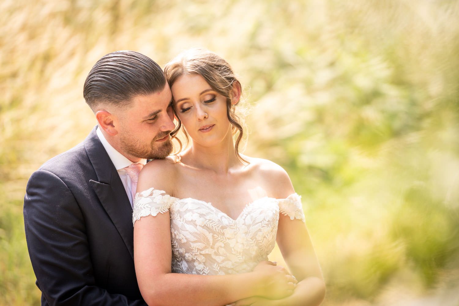 A romantic bridal couple embraces in soft golden sunlight during an intimate outdoor wedding portrait session.