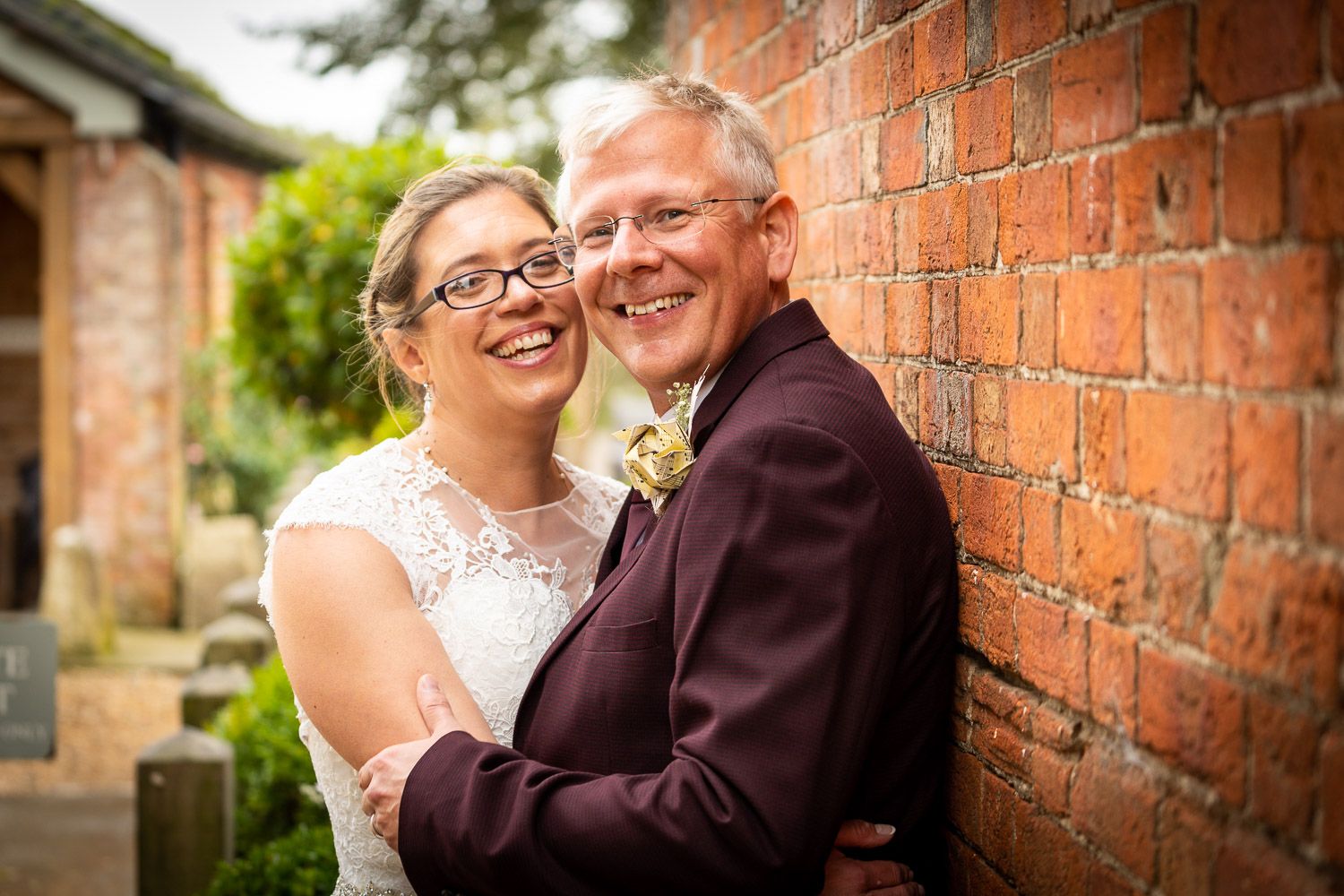 A joyful wedding couple shares a loving embrace against a rustic brick wall on their special day.