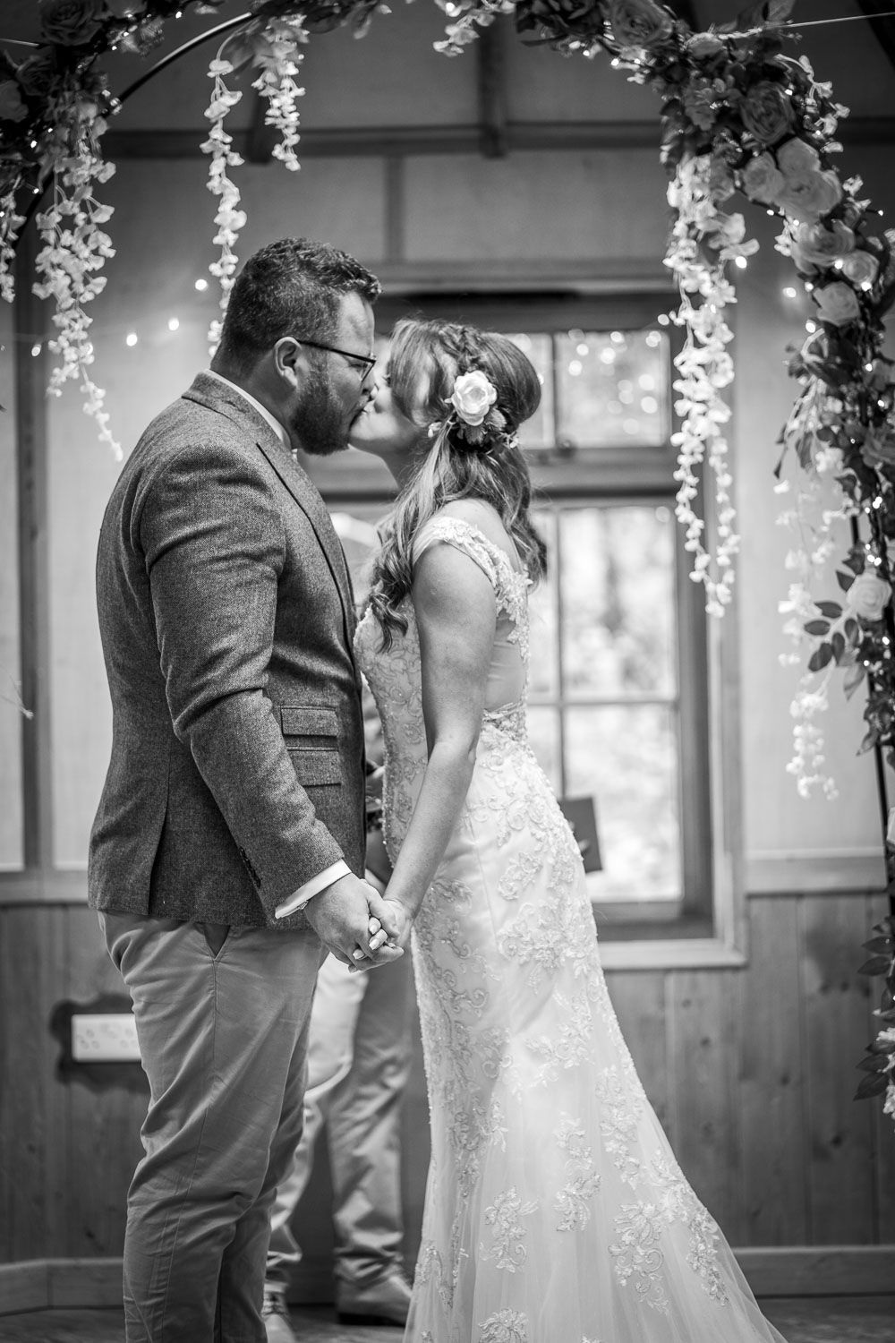 A romantic black and white photo of a couple during their outdoor wedding ceremony under a floral arch.