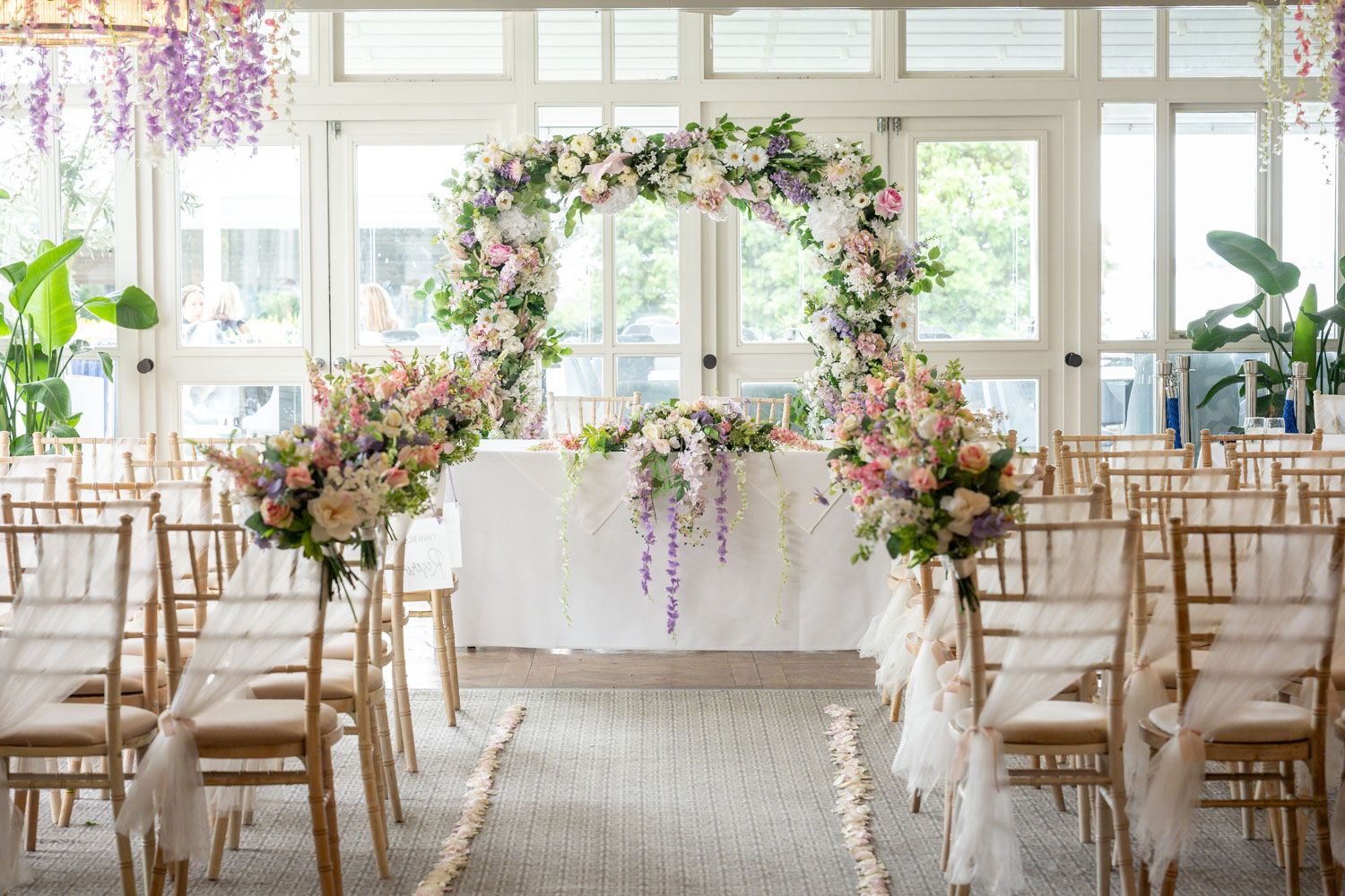 Elegant wedding ceremony setup with floral arch of pink and purple blooms and gold chairs.