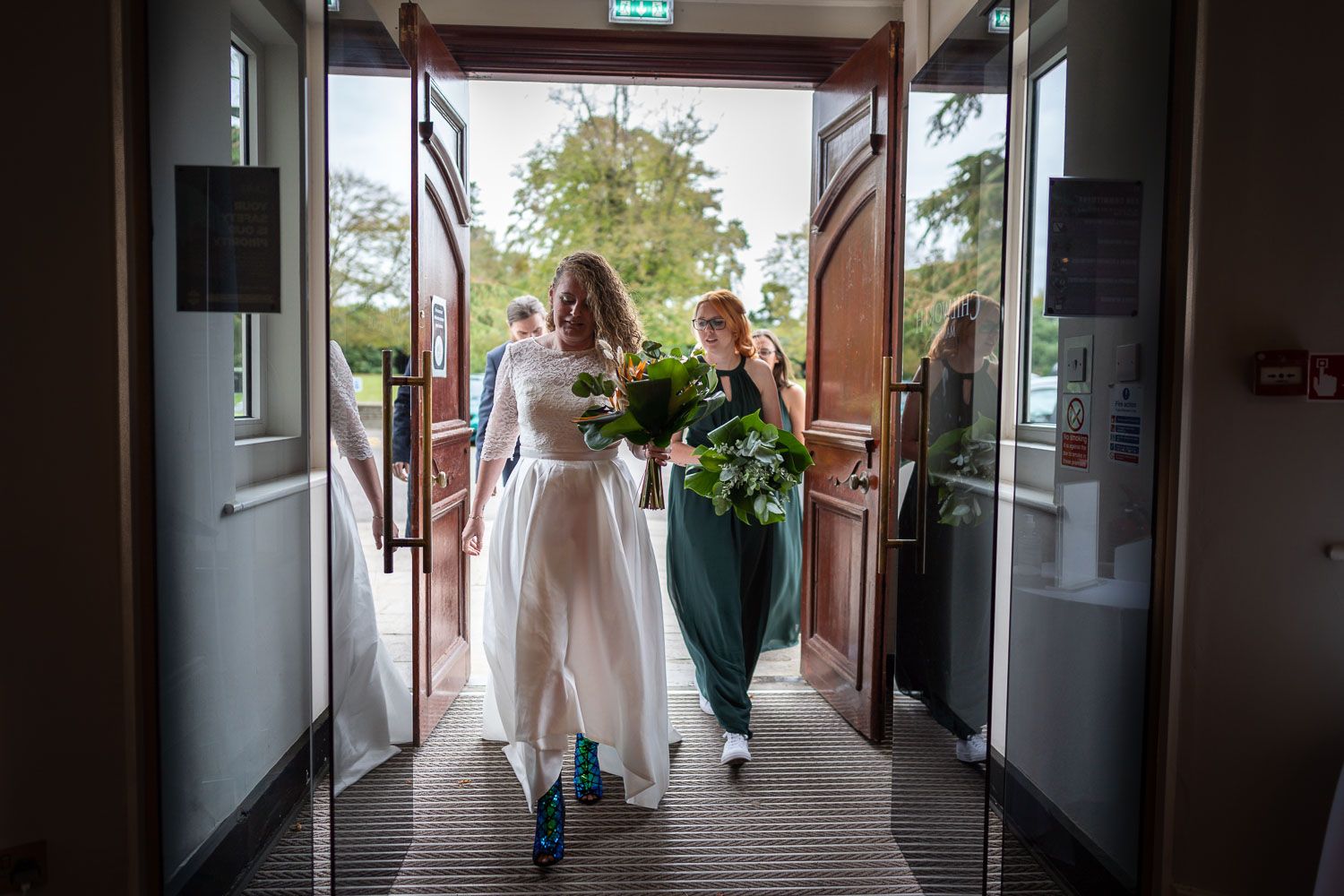 A wedding party walks through doors into a building while carrying bouquets.