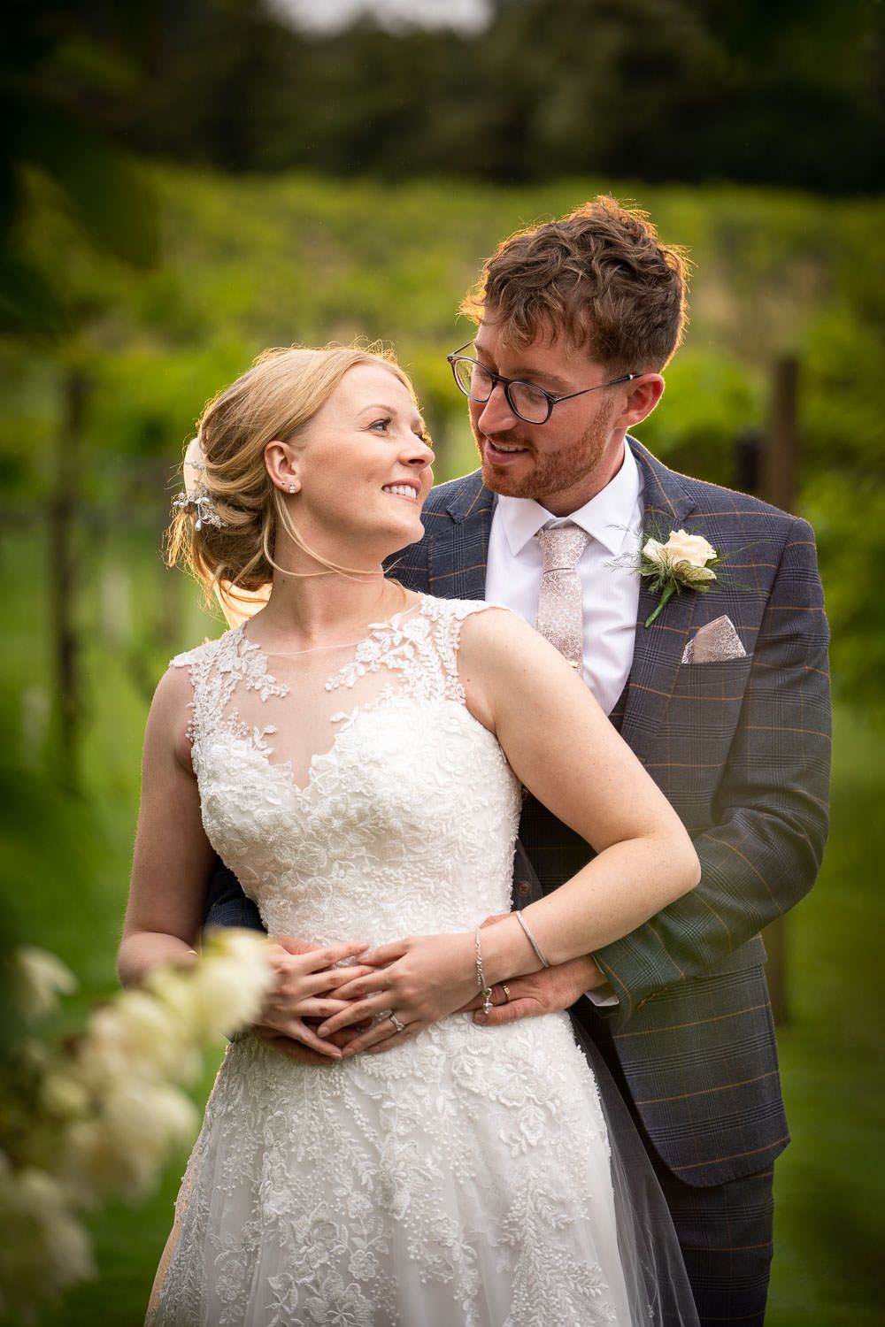 Smiling bride and groom sharing a tender moment in a lush green vineyard setting.