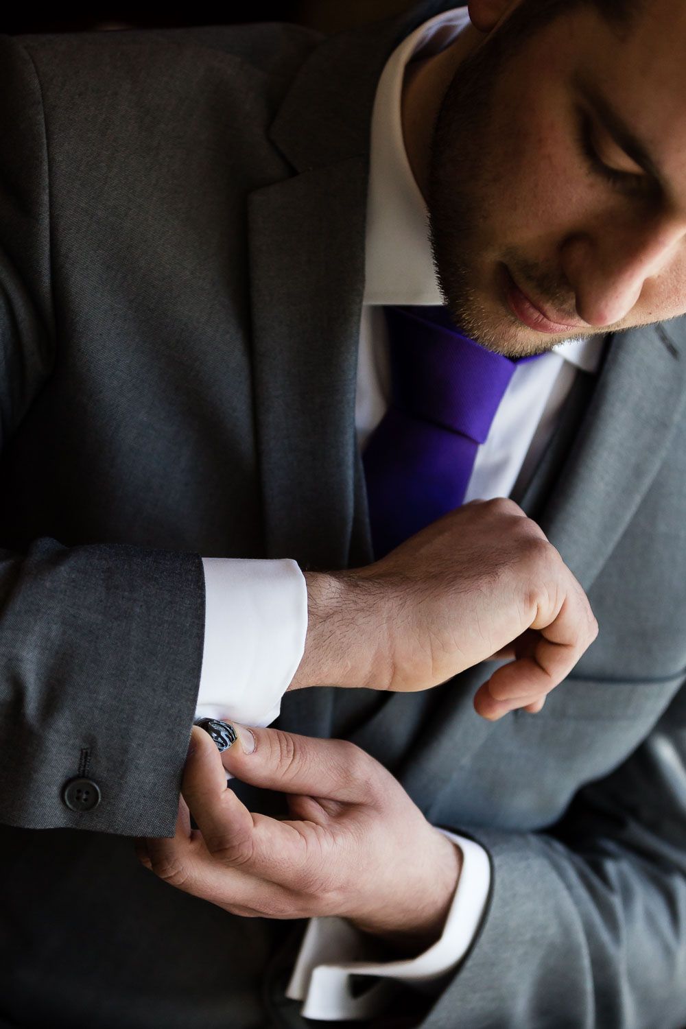 Close-up view of someone adjusting the cuff of a gray suit with a purple tie and white dress shirt.