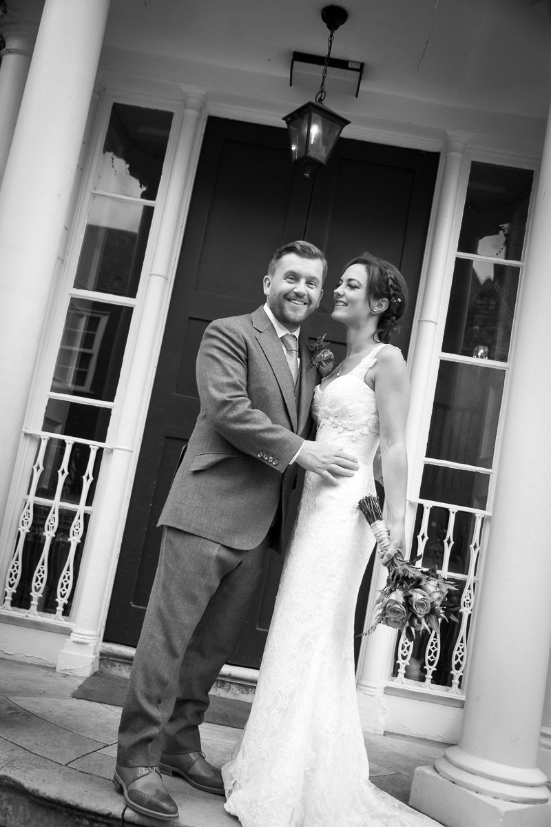 A black and white wedding portrait taken on an elegant porch with white columns and ornate railings.