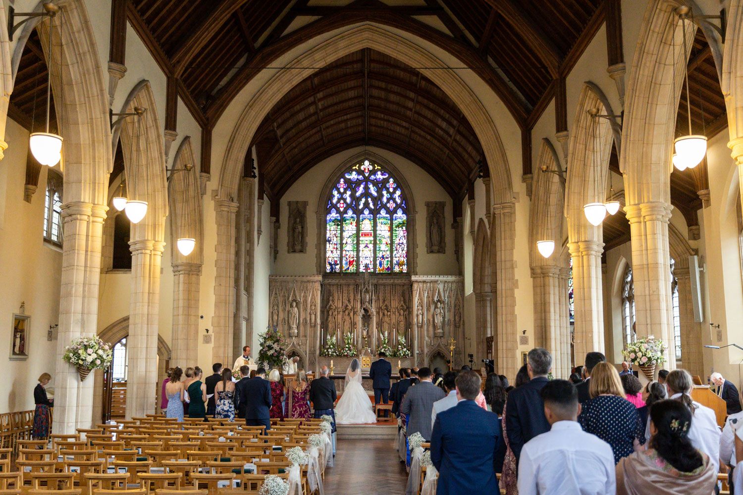Interior of a traditional church with vaulted arches and stained glass windows during a wedding ceremony.