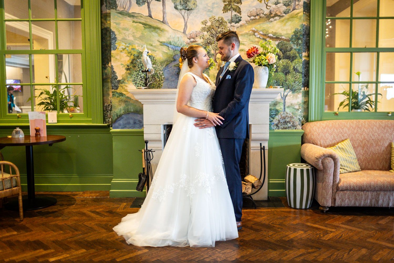 Wedding couple poses in vintage-style room with green walls and painted mural backdrop.