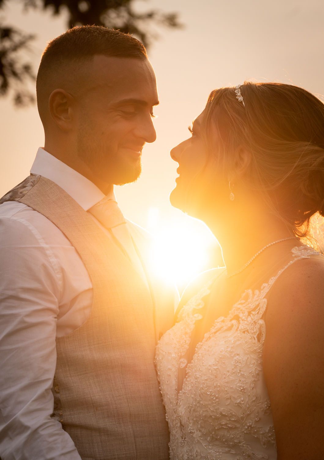 Bride and groom share intimate golden sunset moment, sun glowing between them in warm backlight.