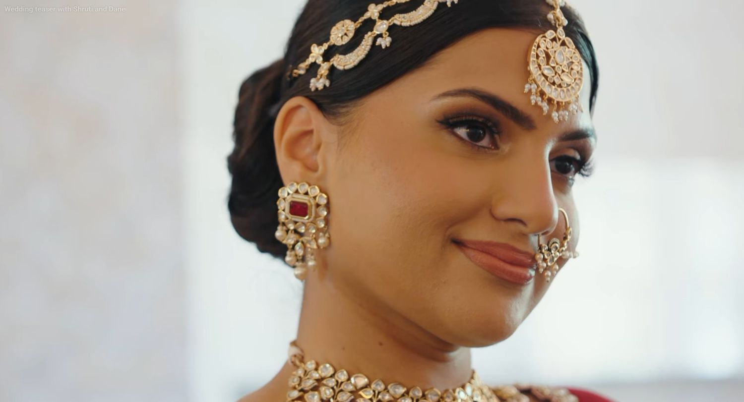 A bride wearing traditional Indian jewelry including a maang tikka, jhumka earrings, nose ring, and kundan necklace.