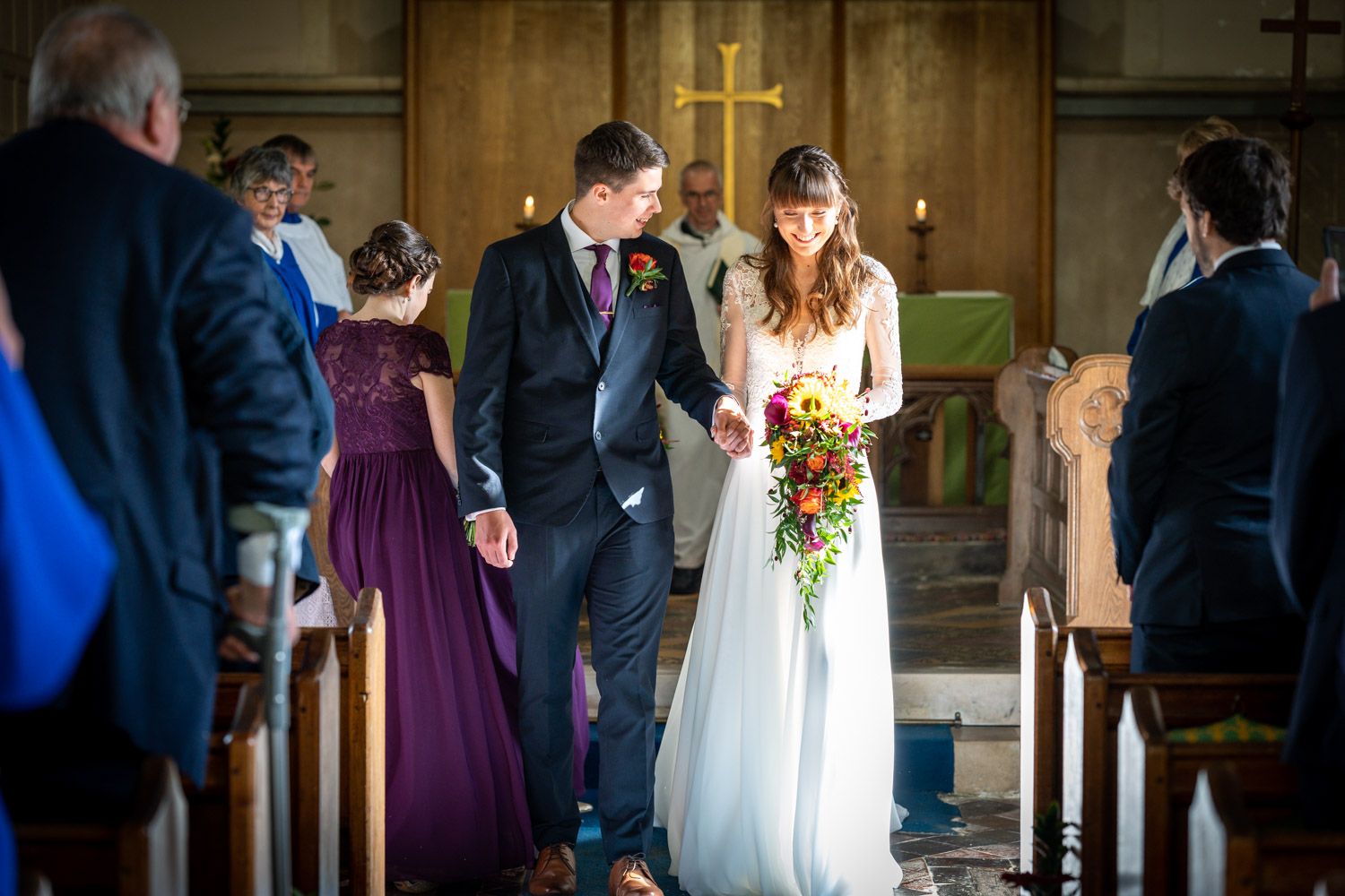 A wedding ceremony takes place in a historic church with stone walls and a warm glow from candles at the altar.