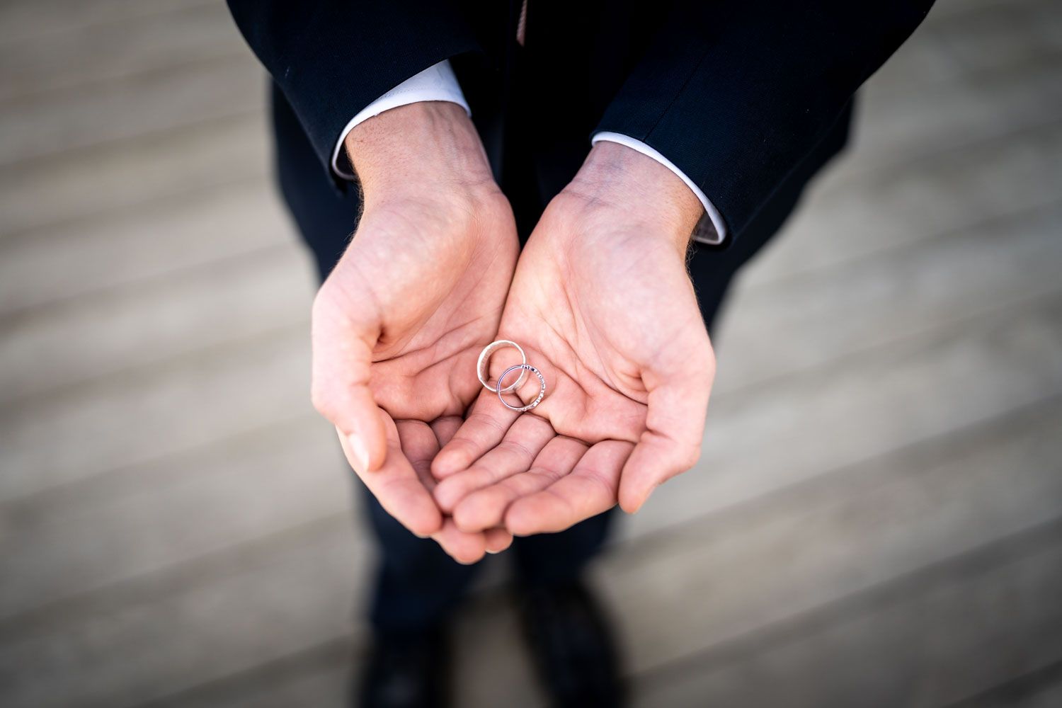 Two open hands held together in a cupped position wearing dark suit sleeves against a blurred grey background.