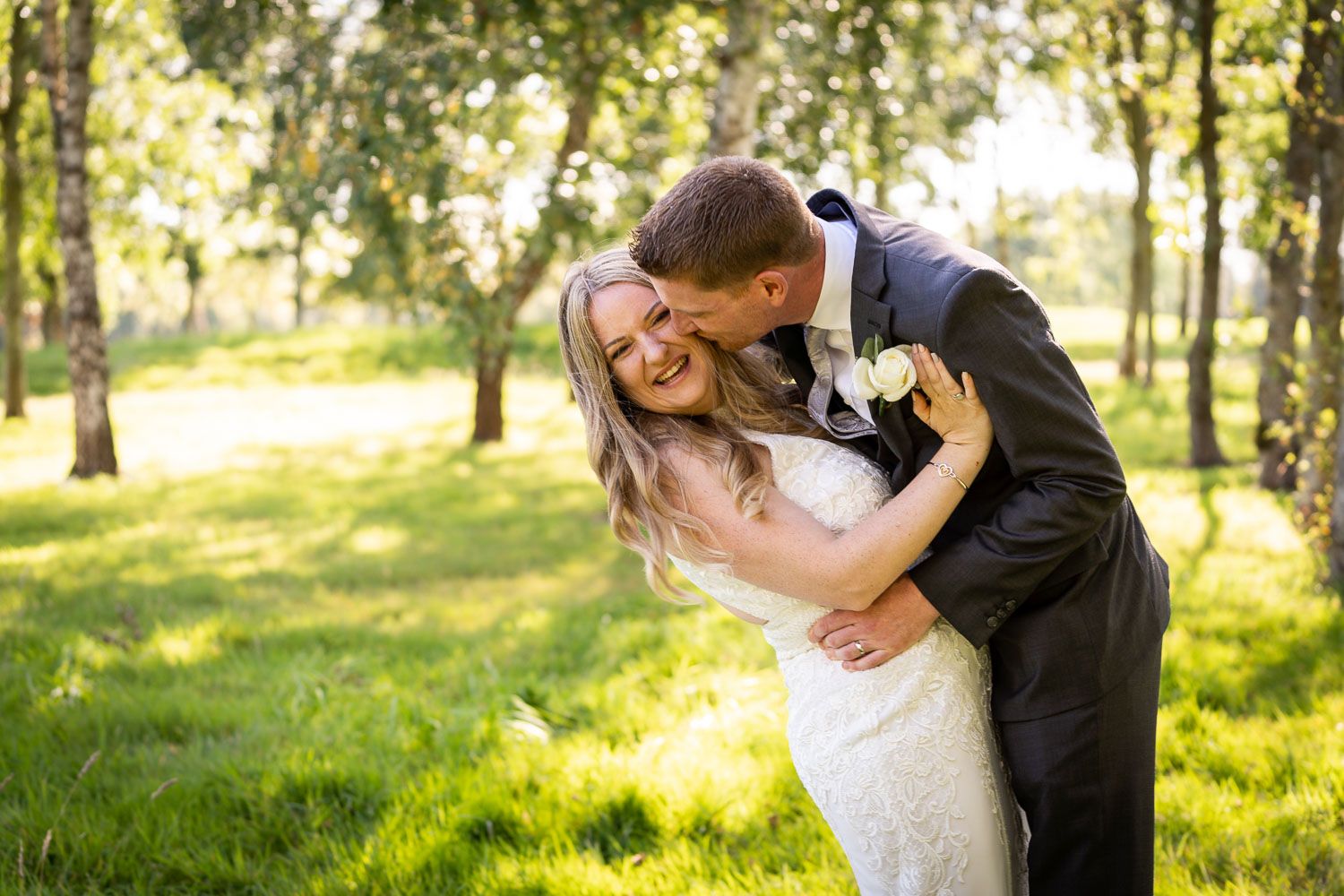 A romantic wedding couple shares a tender moment while dancing in a sunlit park with trees in the background.