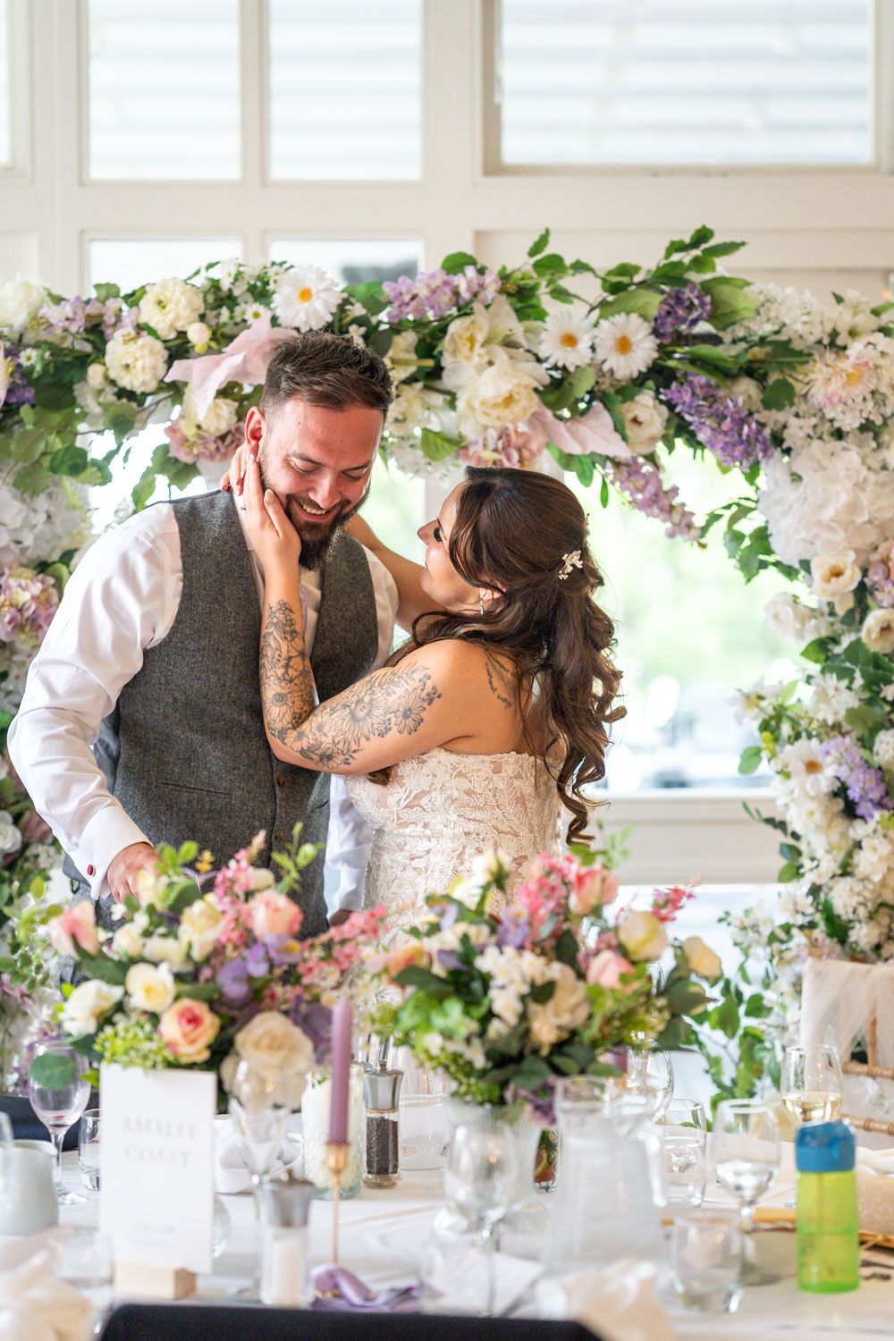 Bride and groom sharing a tender moment beneath a floral arch at their wedding reception.