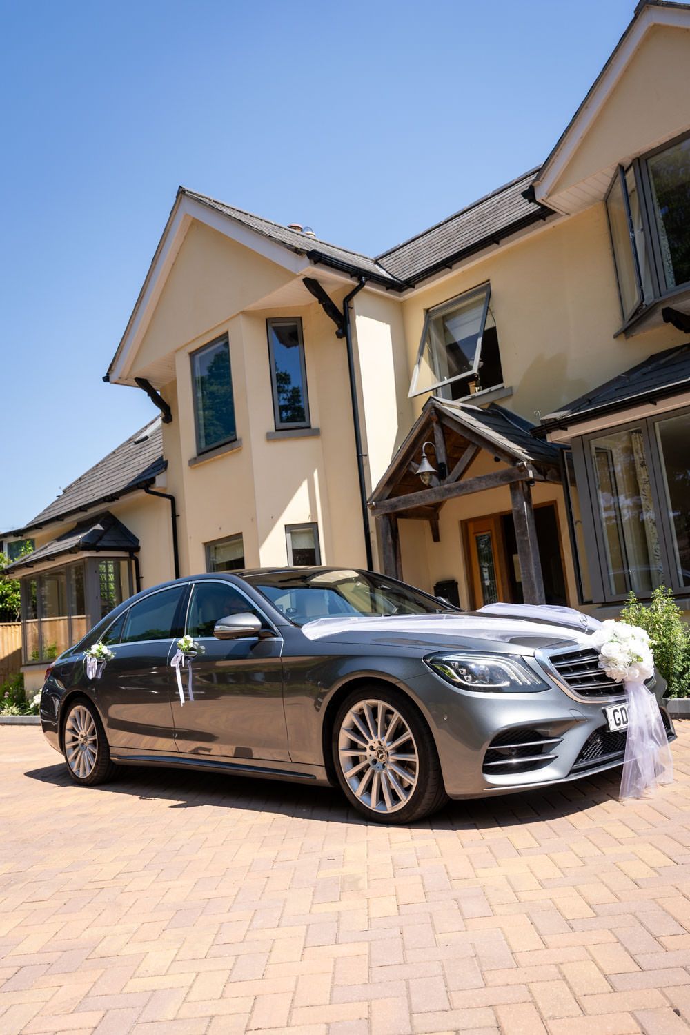 Elegant silver Mercedes-Benz wedding car decorated with white ribbons parked outside a luxury venue.