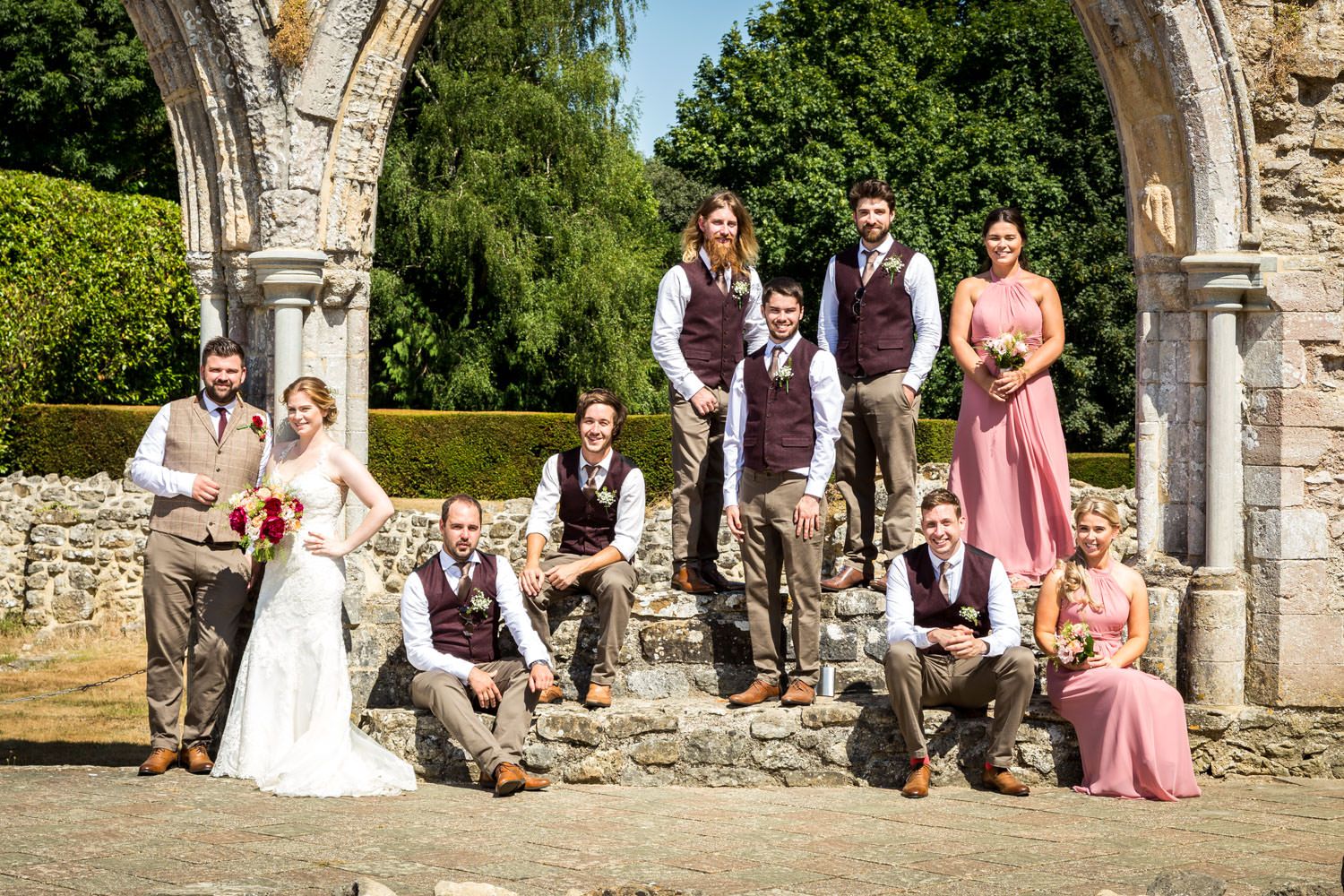 Wedding party poses among ancient stone ruins in sunny outdoor ceremony.