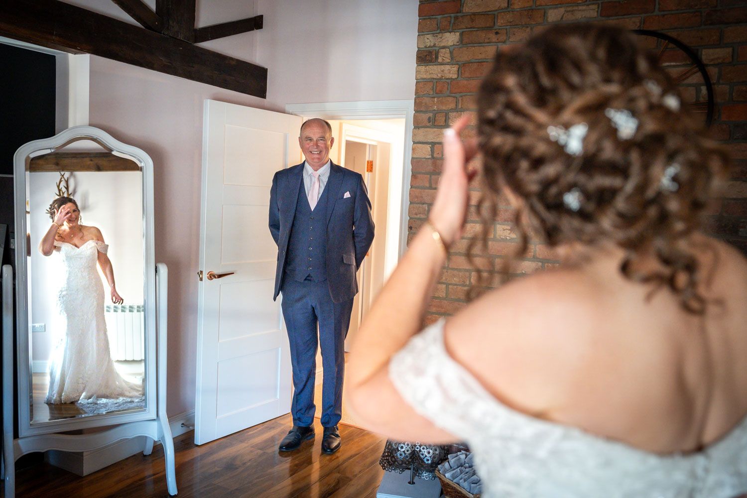 A heartwarming first look moment between a father and bride reflected in an ornate mirror at a wedding venue.