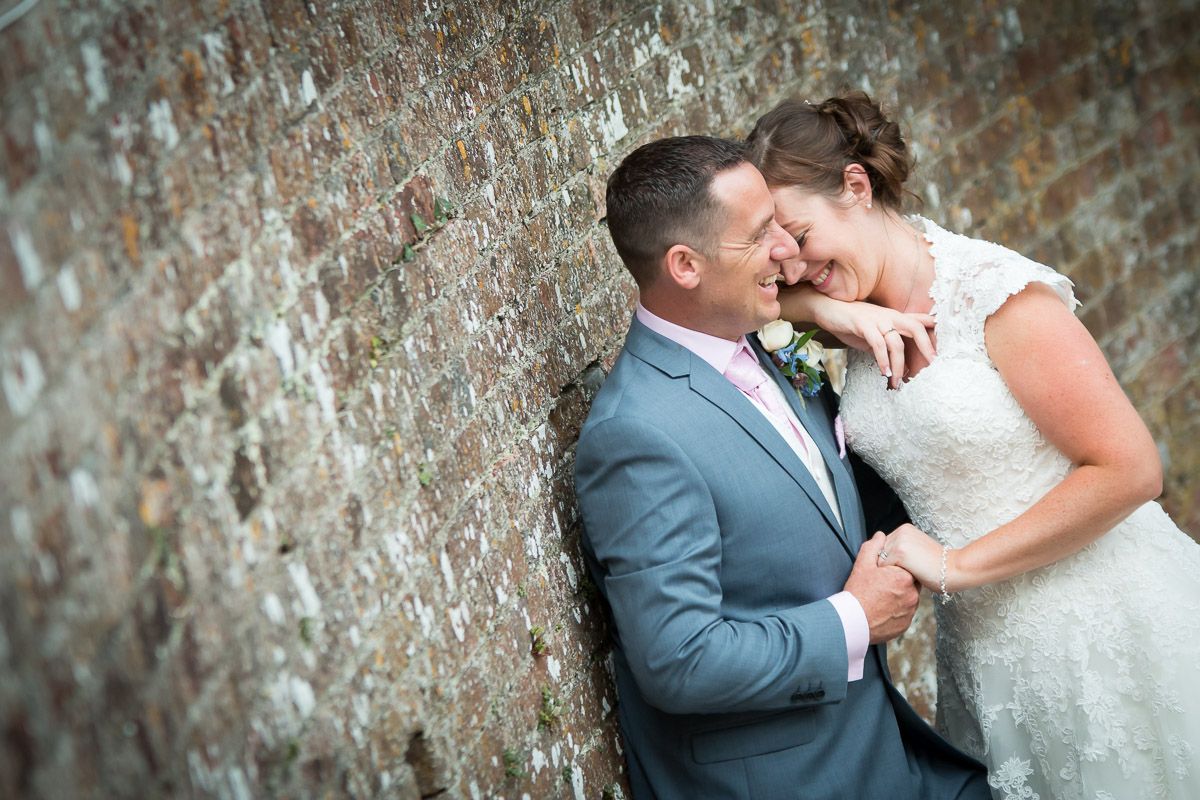 A tender wedding photo features a couple sharing an intimate moment against a rustic stone wall.