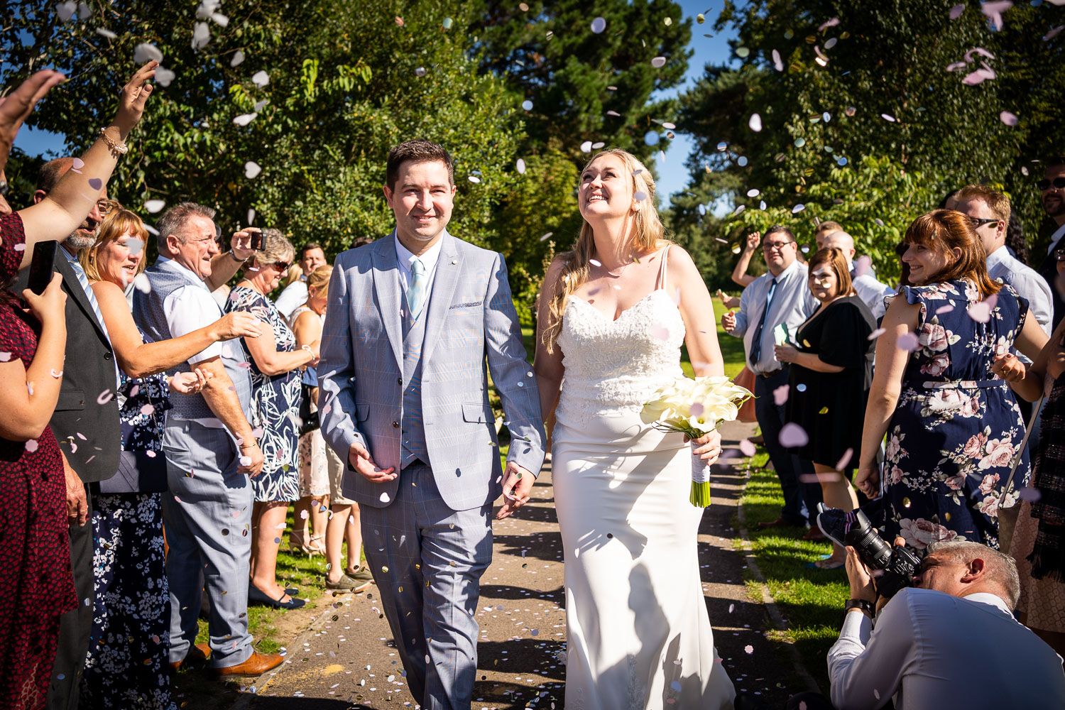 A joyous wedding ceremony recessional with guests throwing confetti along a garden pathway.